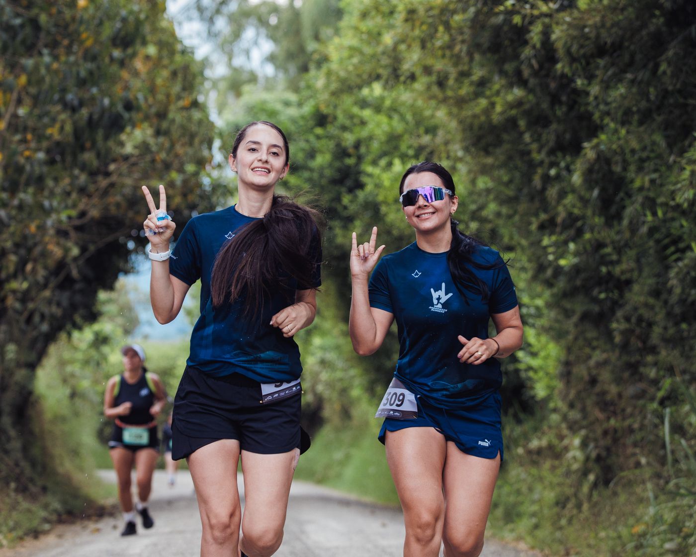 Dos mujeres corriendo y sonriendo en un sendero natural durante una carrera